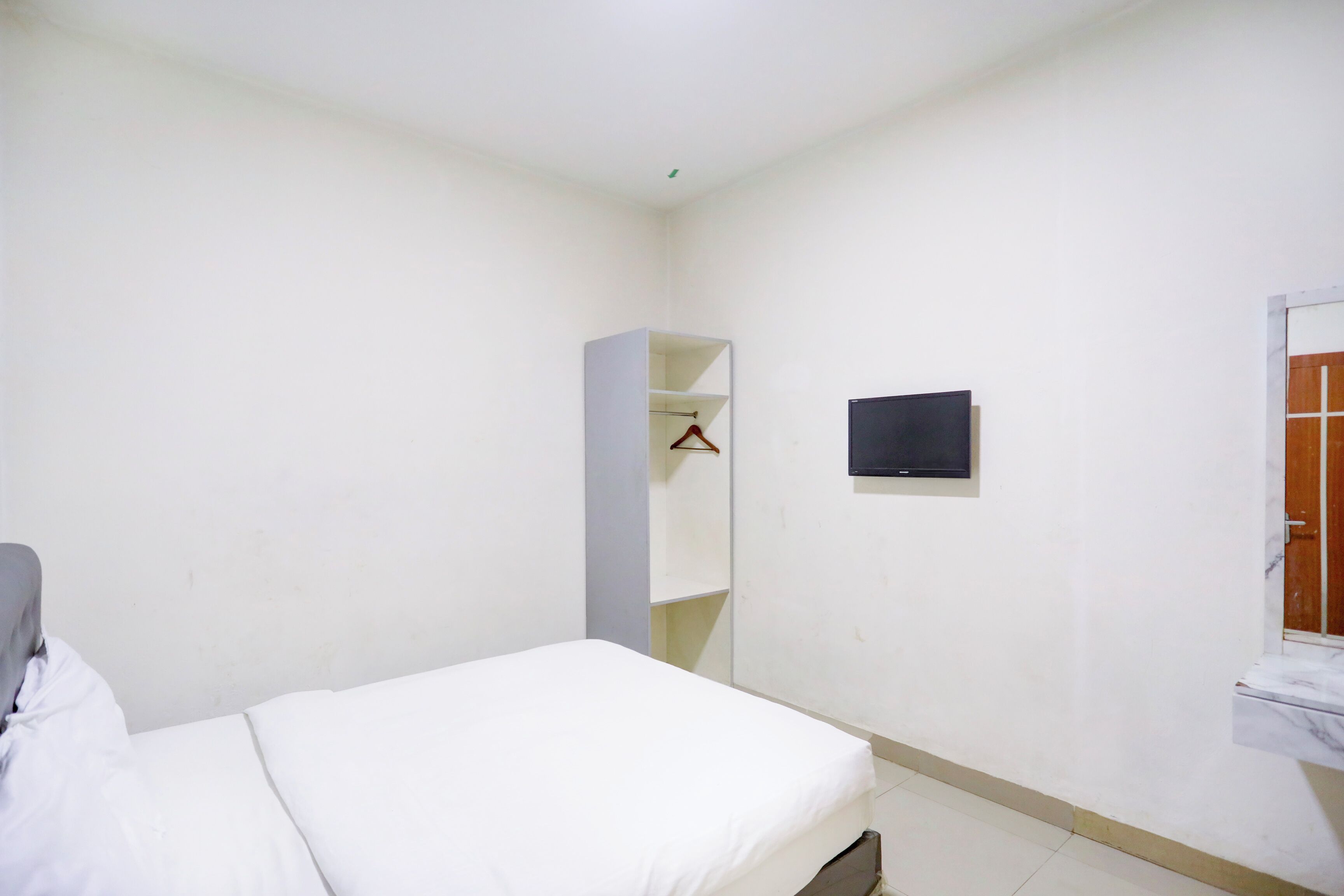 A bedroom with a bed, a wardrobe, a TV mounted on the wall, and a bathroom door.