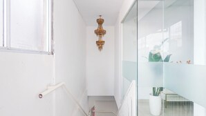 Un couloir étroit aux murs blancs, avec une cloison en verre et un lustre suspendu.