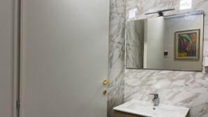 A bathroom with a marble wall, a white sink, and a wooden cabinet. - Deluxe Room – ALH Hotel Digitale (Taranto)