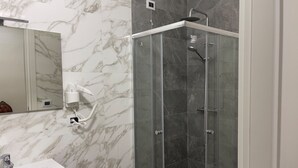 A bathroom with a marble wall, a sink, a mirror, and a glass-enclosed shower area. - Deluxe Room – ALH Hotel Digitale (Taranto)