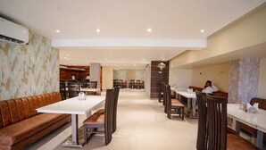 A spacious restaurant with high tables and booths, a central bar area, and a patterned wall on one side. - Hotel Mezbaan  (Raipur)