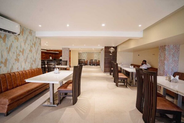 A spacious restaurant with high tables and booths, a central bar area, and a patterned wall on one side. - Hotel Mezbaan (Raipur)