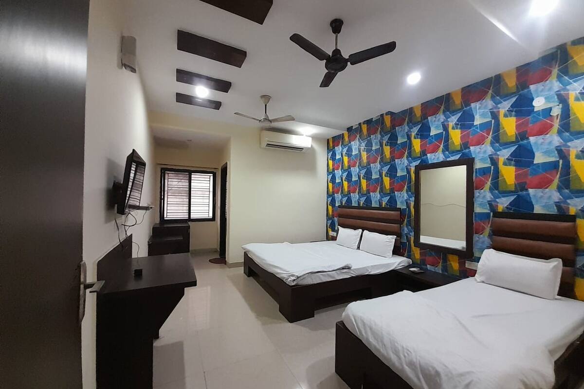 A hotel room with two beds, a desk, a ceiling fan, and a colorful geometric wall design.