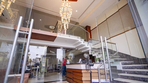 A modern lobby with a glass staircase, a reception desk, and a chandelier. - Hotel Mezbaan  (Raipur)