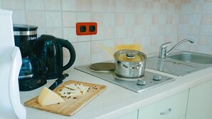 Une cuisine équipée d’une machine à café, d’une casserole de spaghettis, d’une planche à découper avec du fromage et d’un évier.