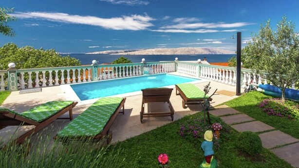 Une piscine avec vue sur la mer, entourée d’un jardin agrémenté d’une clôture et de chaises longues.