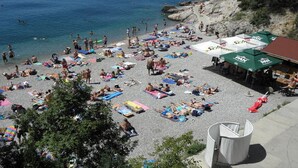 Une plage bondée où les gens se prélassent au soleil et se baignent, avec plusieurs parasols et tables.