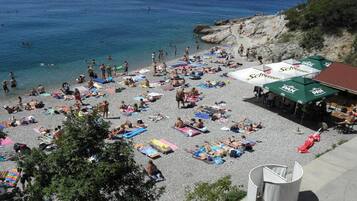 A crowded beach with people sunbathing and swimming, and several beach umbrellas and tables.