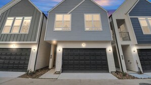 Una serie di tre case a due piani con garage integrati, ciascuna con un portico anteriore e illuminazione esterna.