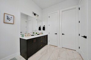 Une salle de bain avec un meuble-lavabo noir, des murs blancs, un grand miroir et deux portes blanches.
