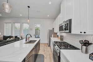 Une cuisine moderne avec des meubles blancs, un îlot central, des appareils en acier inoxydable et une vue sur l’extérieur.