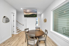 Uma sala de jantar moderna com uma mesa redonda, quatro cadeiras, uma TV de tela plana na parede e uma escada que leva a outro nível.