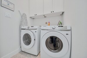 Un espace buanderie comprenant deux machines à laver blanches, un porte-serviettes blanc et un meuble blanc placé au-dessus.