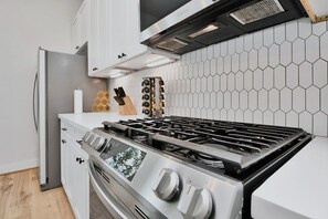 Una cucina con piano cottura in acciaio inossidabile, mobili bianchi, rivestimento a mosaico esagonale e design moderno.
