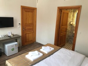 Een hotelkamer met een bed, een bureau met een koelkast, een televisie en houten deuren.