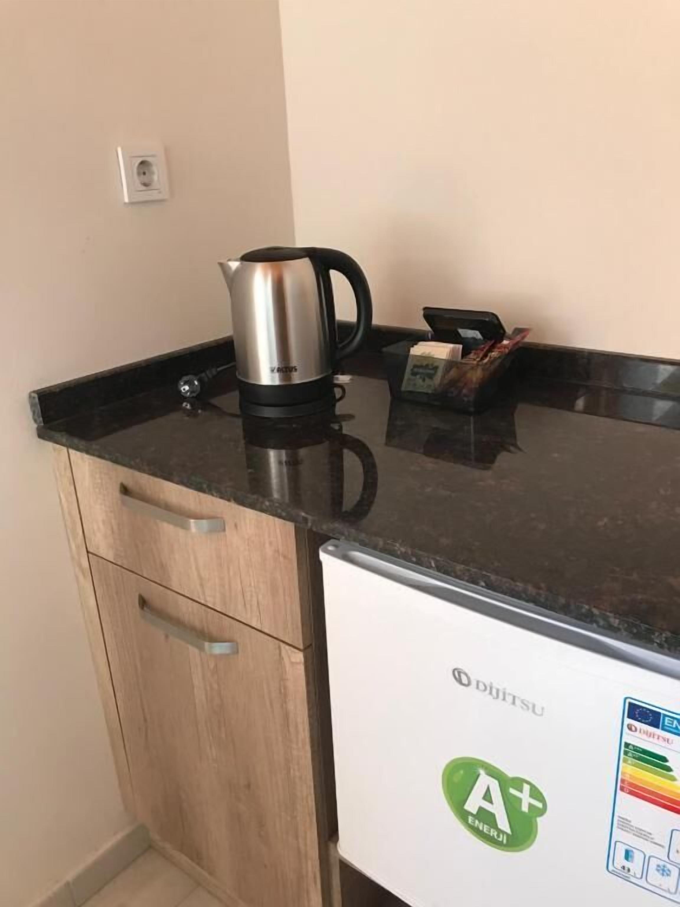 A kitchenette with a stainless steel kettle, a coffee maker, and a box of tissues on the countertop.