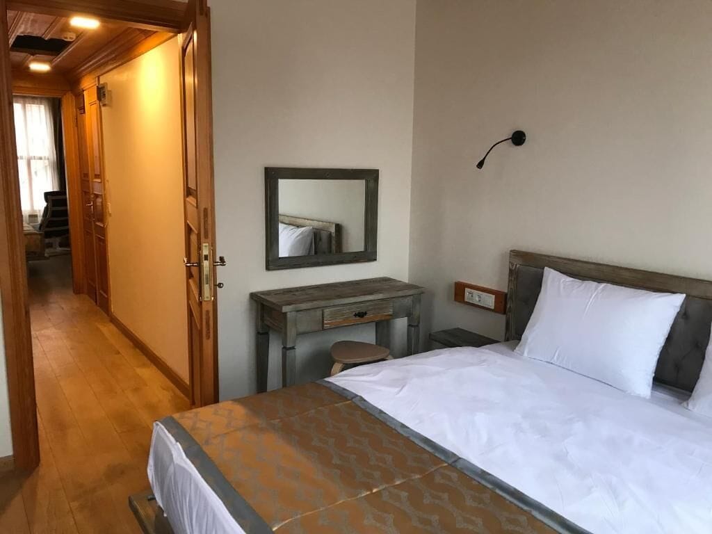 Een hotelkamer met een bed, bureau, stoel, spiegel en nachtkastje.