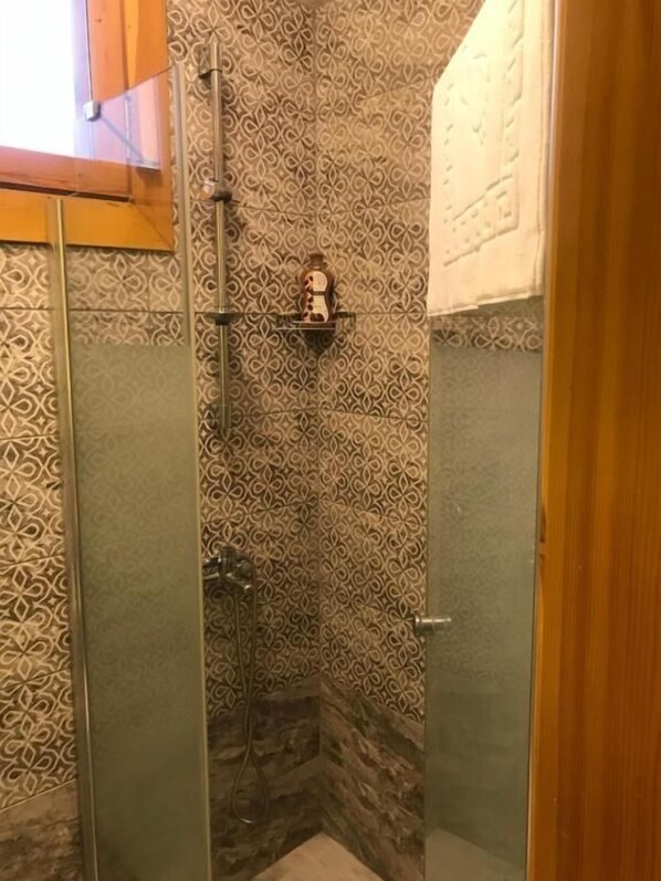 A shower with patterned tiles, a glass door, and a shelf with toiletries. - Green Mansion (Istanbul)
