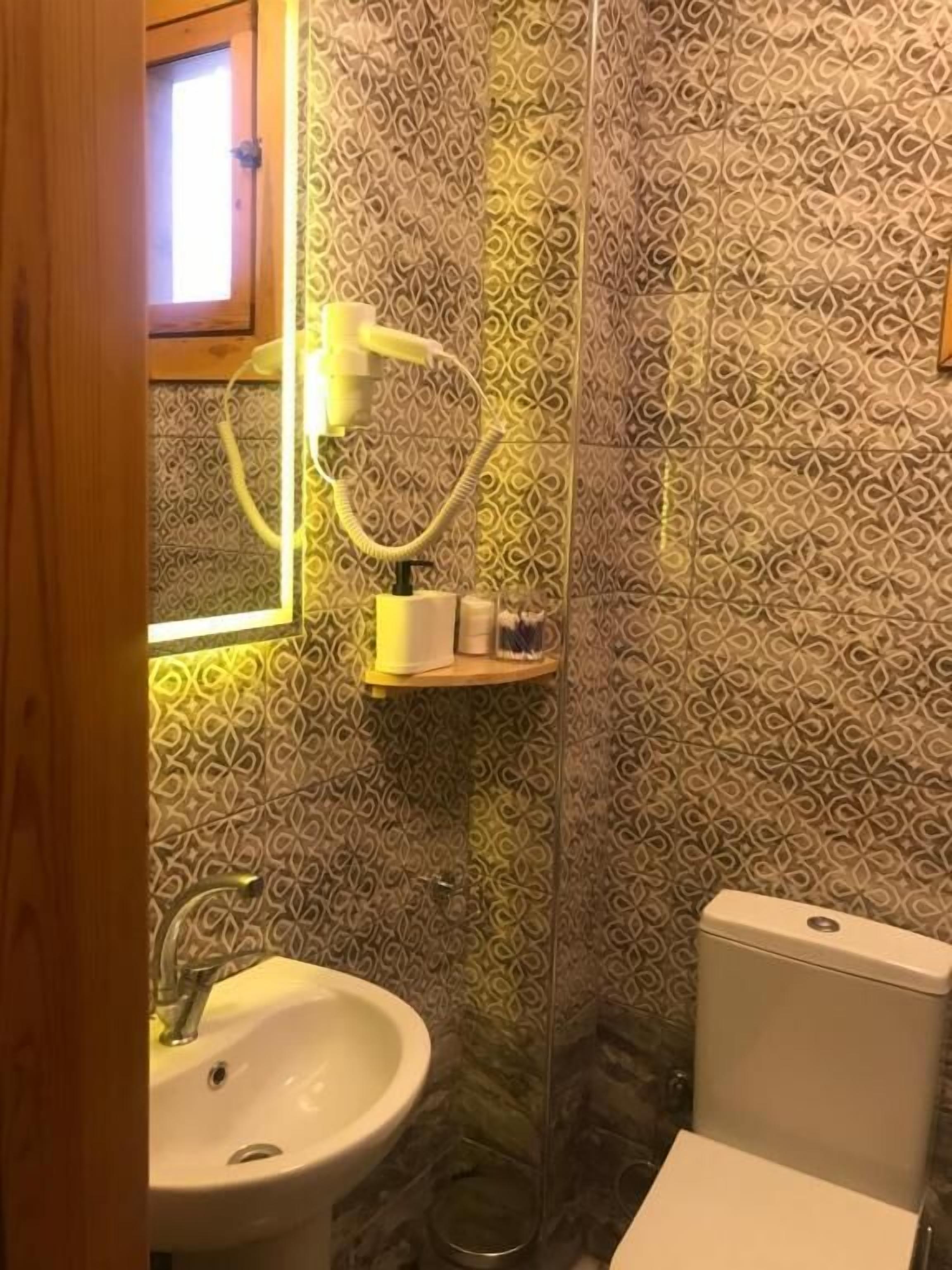 A bathroom with patterned tiles, a sink, a toilet, and a shelf with toiletries.