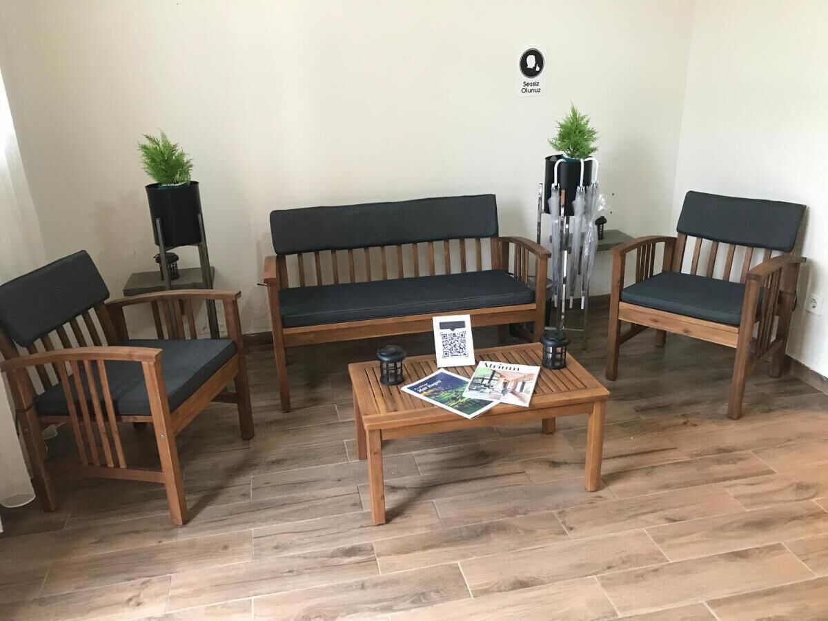 A room with a wooden floor, a sofa, two wooden chairs, a small table with a QR code, and two potted plants.