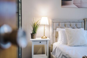 A neatly made bed with white bedding and a tufted headboard, a bedside table with a lamp and a potted plant, and a wall-mounted artwork above the bed. - 3br-sleeps6-garden-bbq-freeparking-pets (Salford)