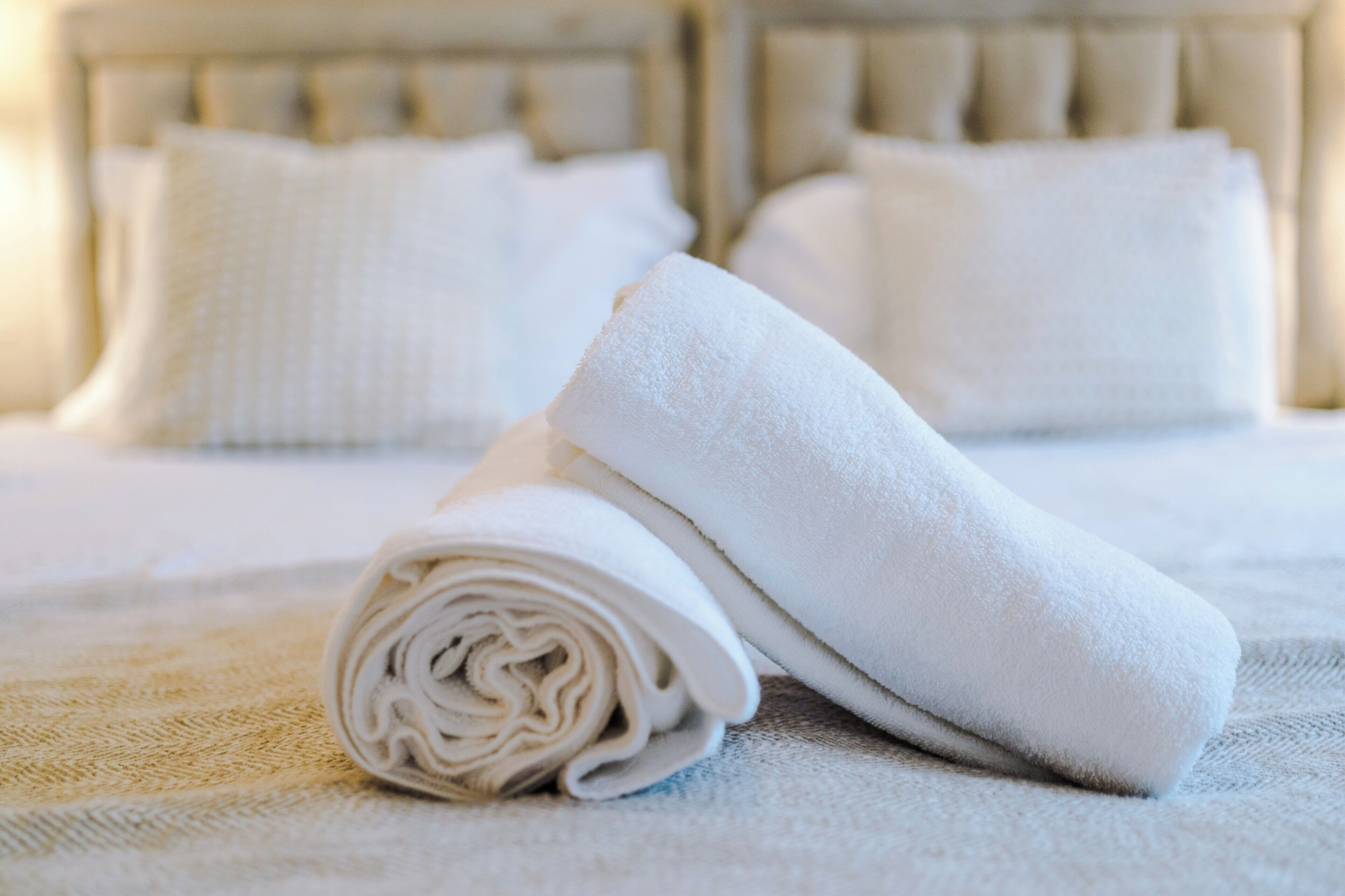 A neatly made bed with white linens and pillows, a rolled-up towel, and a textured blanket.