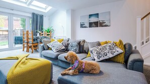 A living room with a sofa, a dog, and a table with chairs. - 3br-sleeps6-garden-bbq-freeparking-pets (Salford)