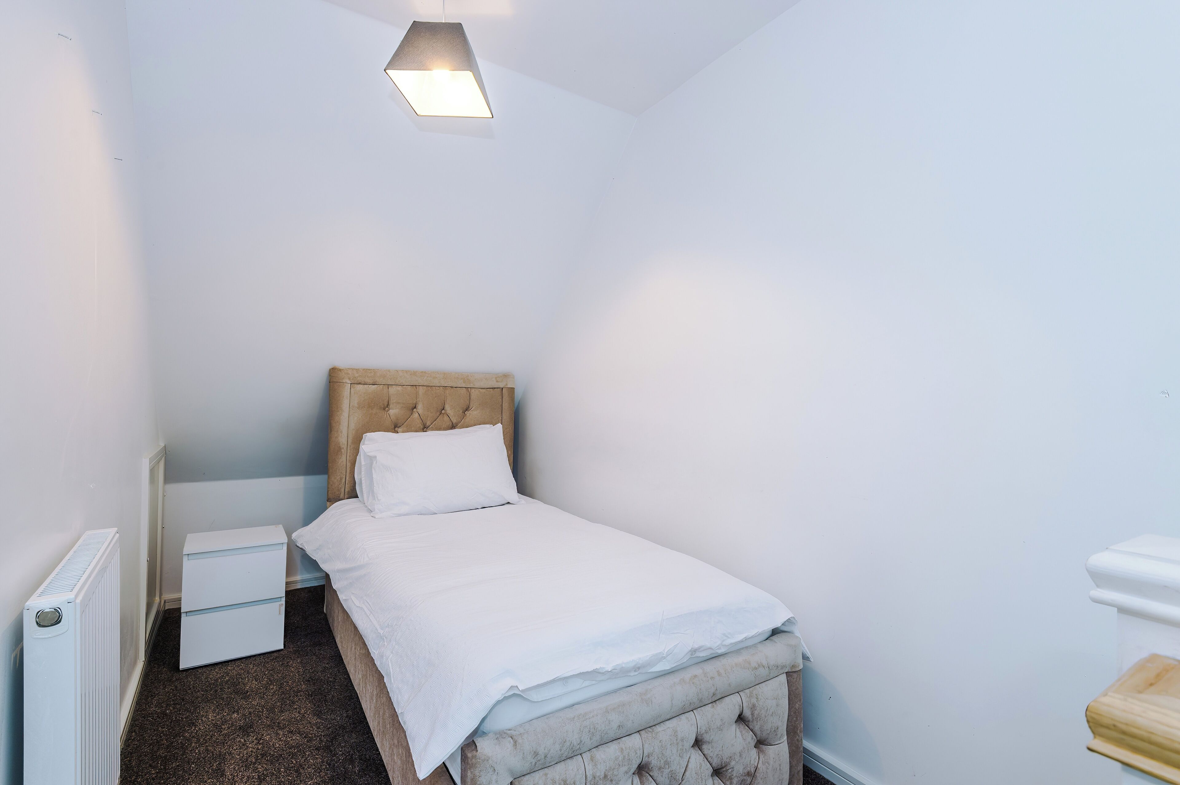Ein kleines, ordentlich eingerichtetes Schlafzimmer mit einem Einzelbett, einem Nachttisch und einer Heizung.