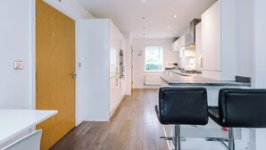 A modern kitchen with white cabinets, a wooden door, and a dining area with black chairs. - 3br-walktocitycentre-garden-freeparking (Salford)