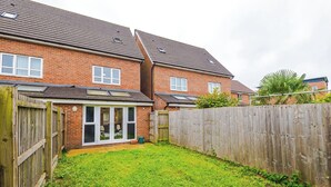 A residential backyard with a brick house, a wooden fence, and a grassy lawn. - 3br-walktocitycentre-garden-freeparking (Salford)