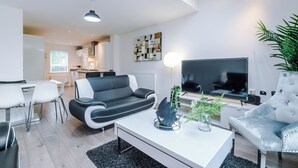 A modern living room with a black and white sofa, a flat-screen TV, and a dining area with white chairs. - 3br-walktocitycentre-garden-freeparking (Salford)
