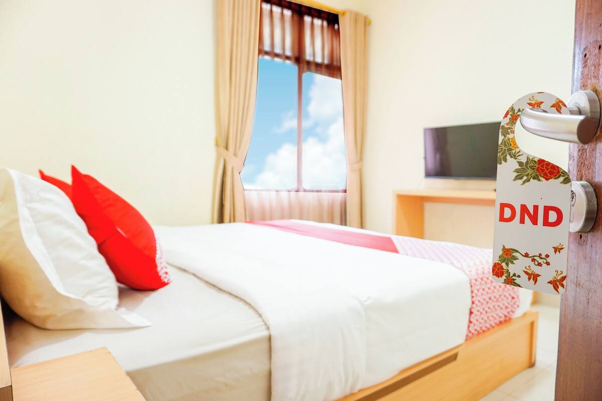 Une chambre à coucher avec un lit, des oreillers, une télévision et une fenêtre avec des rideaux.