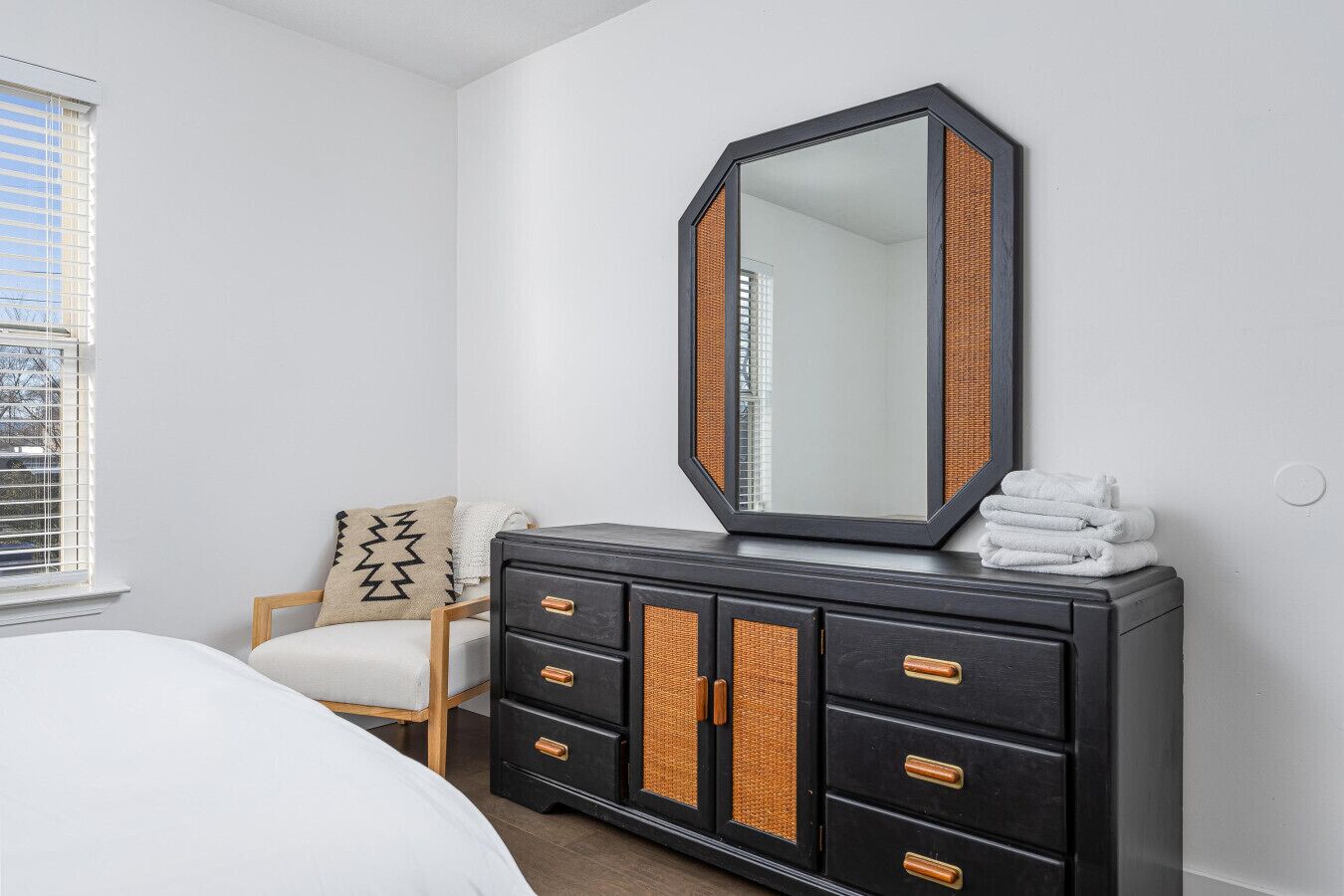 A bedroom with a bed, a dresser with a mirror, and a window with blinds.