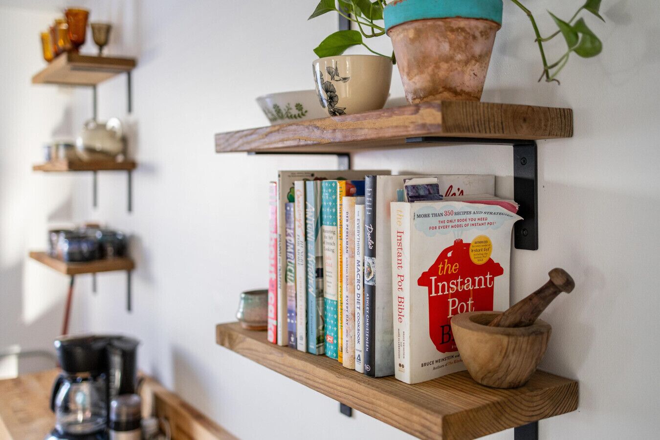 A kitchen shelf with cookbooks, a coffee maker, and a wooden mortar.