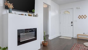 Een woonkamer met een open haard, een aan de muur bevestigde televisie en een deur met een decoratief glasraam.