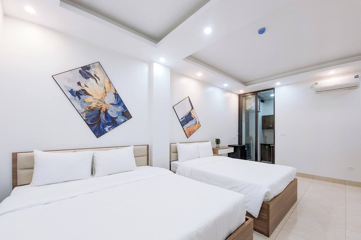 A hotel room with two beds, a small bedside table with a plant, and a glass shower enclosure.