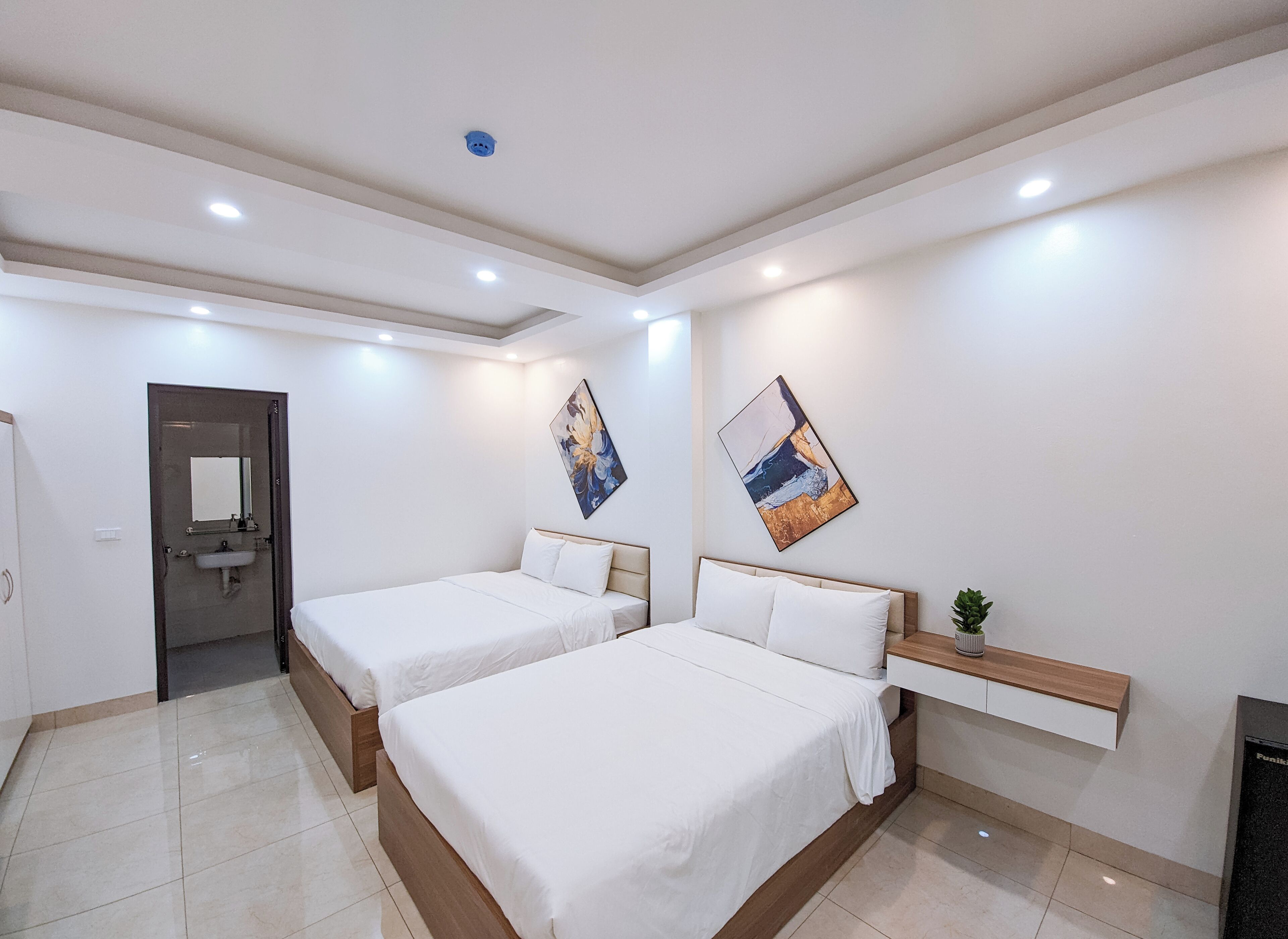A hotel room with two beds, a built-in bench, a sink, and a ceiling-mounted light fixture.