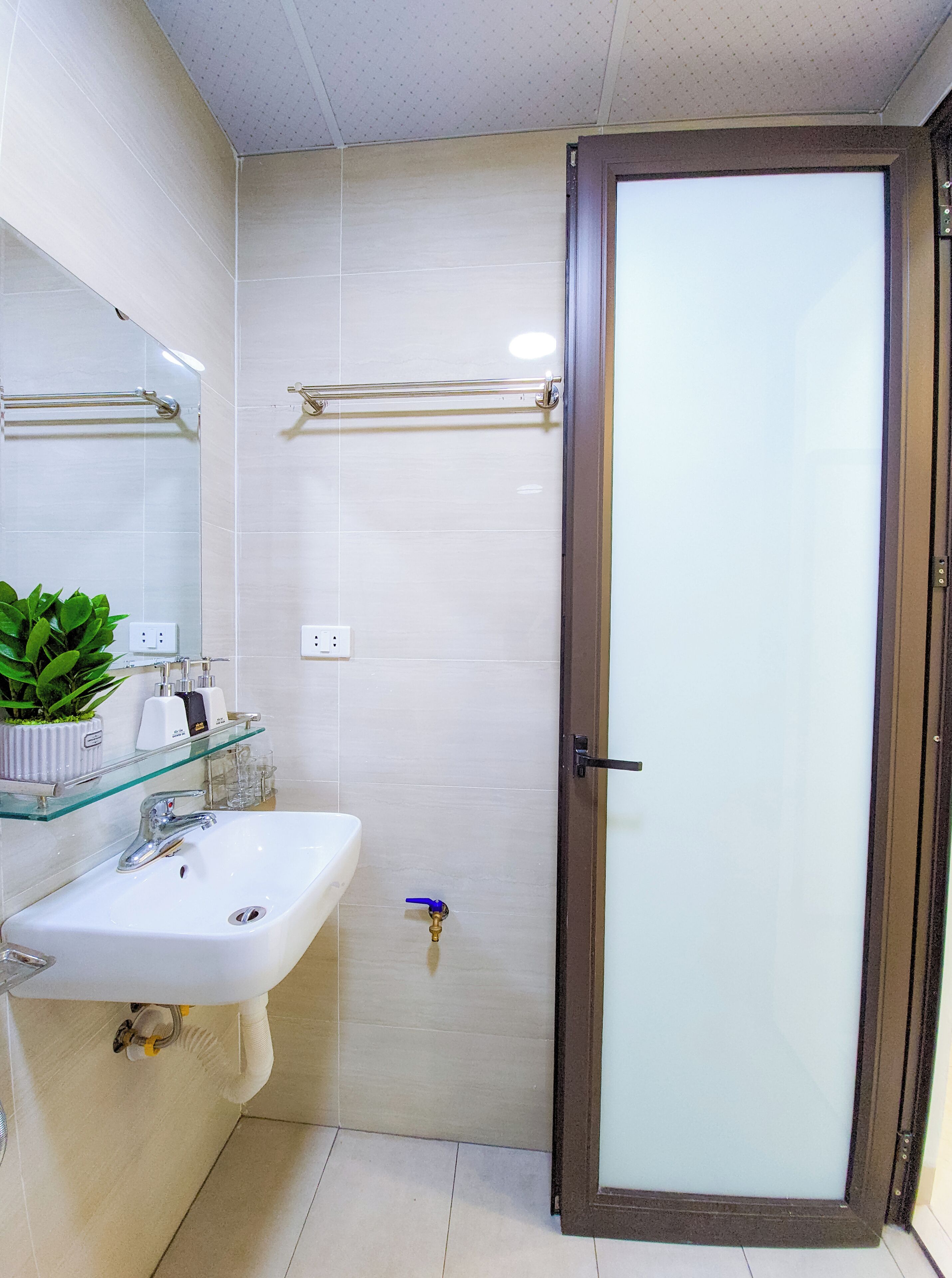 A bathroom with a glass shower enclosure, a white sink, and a glass shelf with toiletries.