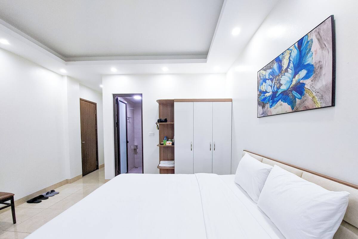 A modern bedroom with a large bed, a wardrobe, a shower area, and a painting on the wall.