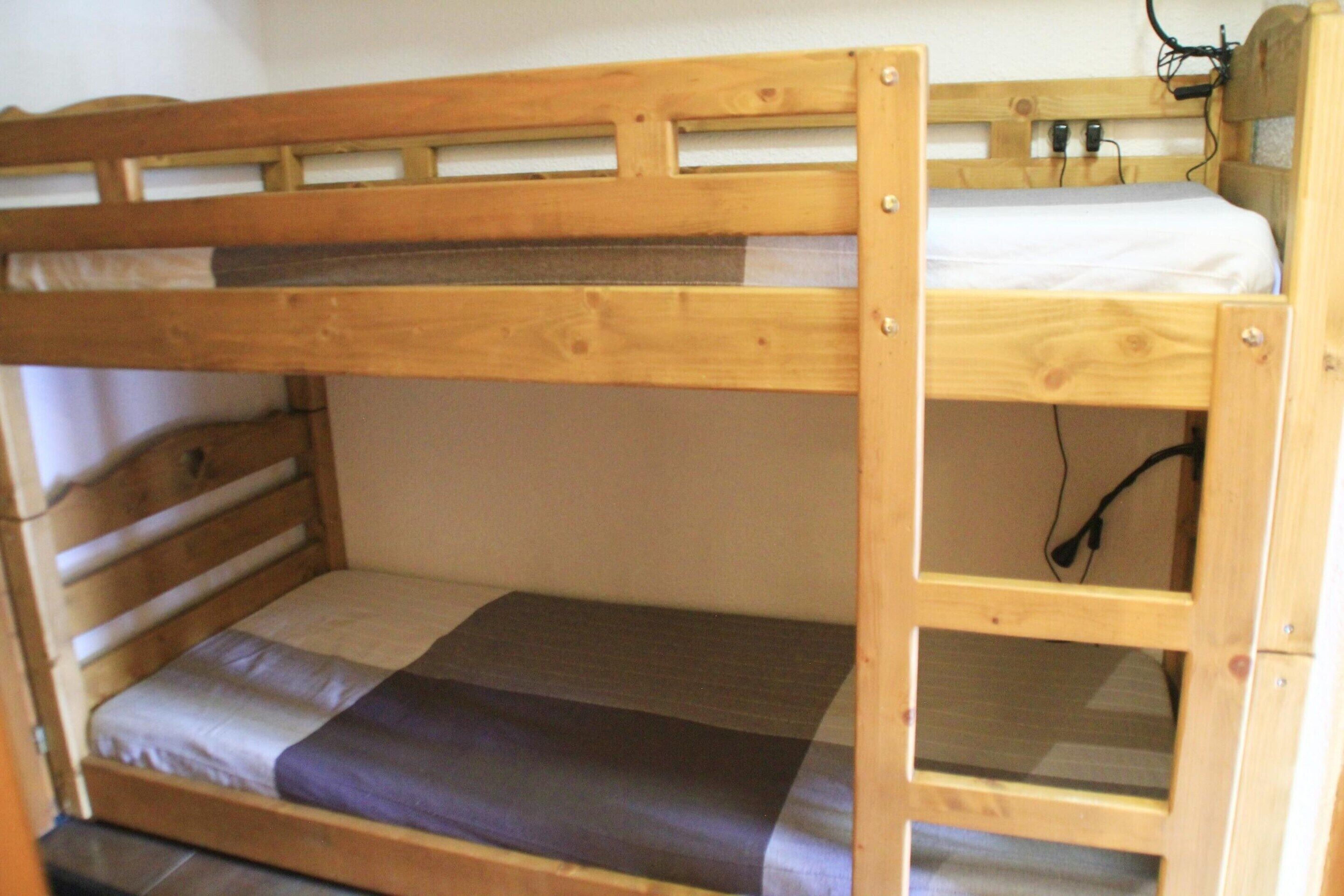 A bunk bed with a wooden frame, a mattress, and a blanket.