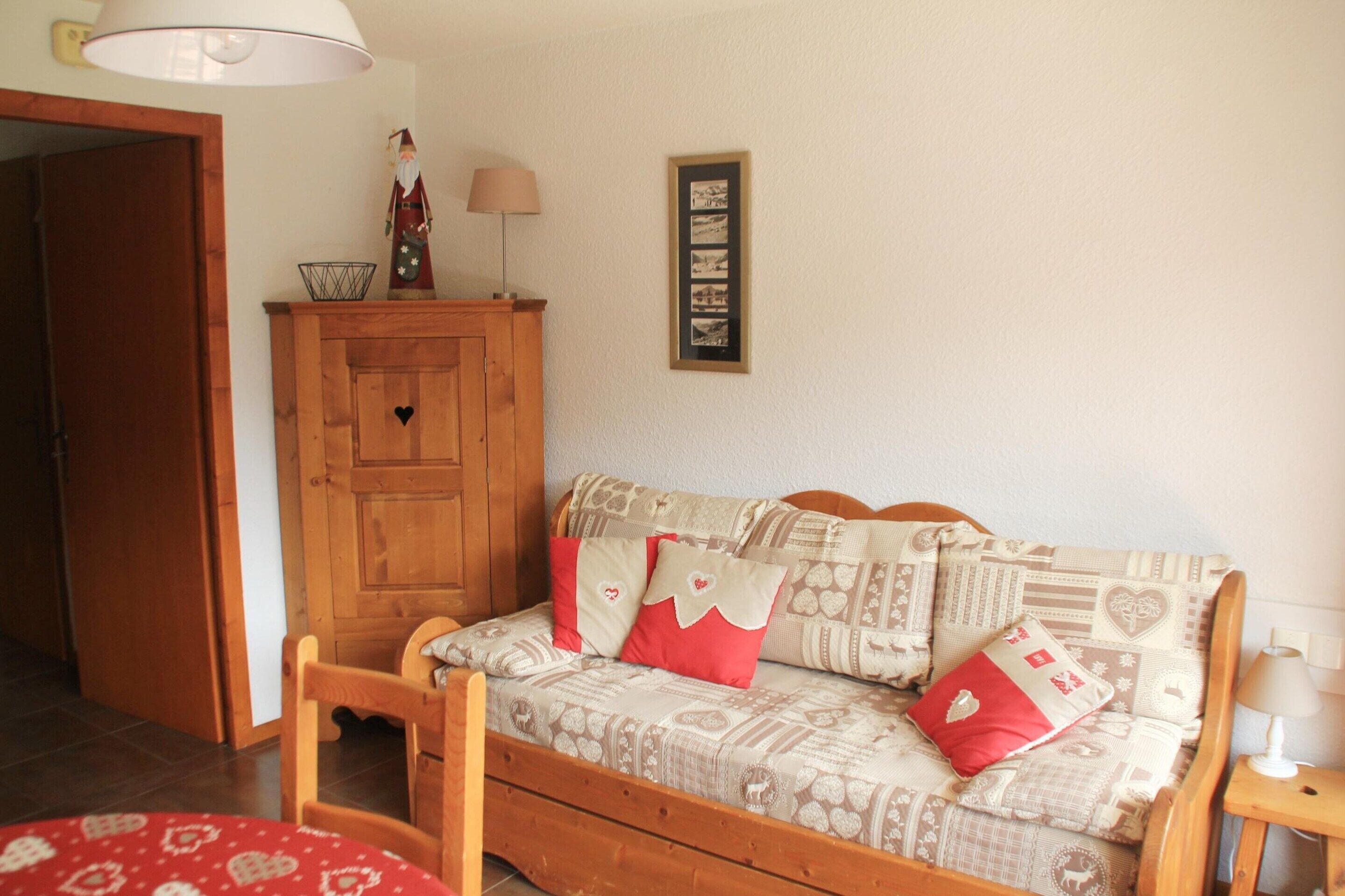 A cozy room with a wooden sofa, a small cabinet, a framed photo, and a lamp.