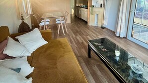 A hotel room with a sofa, a glass coffee table, a dining area with a table and chairs, and a kitchen area. - Vakantiepark Klein Vink - 25 (Arcen)