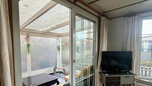 A room with a sliding glass door leading to an outdoor area, a sofa, a small table, and a television on a stand. - Vakantiepark Klein Vink - 25 (Arcen)