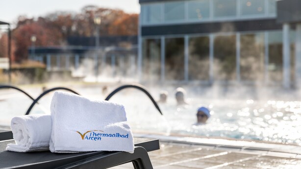 A pool area with a towel labeled "The Arcelia" and a modern building in the background. - Vakantiepark Klein Vink - 25 (Arcen)