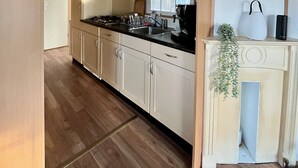 A modern kitchen with wooden flooring, white cabinets, a black countertop, and a window providing natural light. - Vakantiepark Klein Vink - 25 (Arcen)