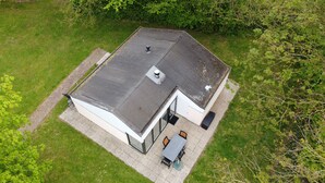 Vista aérea de una casa moderna con techo inclinado, un patio con mesa y sillas, y un pequeño jardín.