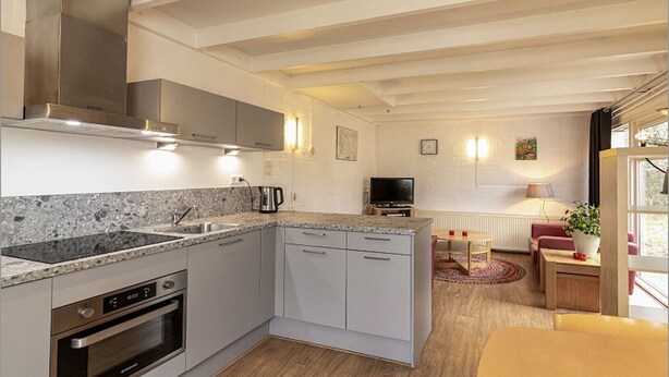 Una cocina moderna con electrodomésticos integrados, un comedor con mesa y sillas, y un espacio de sala de estar con sofá y televisor.