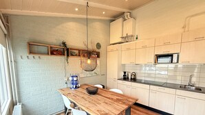 A modern kitchen with wooden cabinets, a built-in microwave, and a dining area with a wooden table and white chairs. - Bungalowpark Simpelveld - Schakel 22 (Simpelveld)