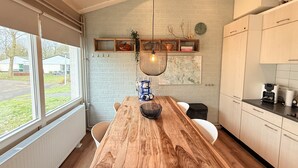 A modern kitchen with a wooden table, white cabinets, and a view of the outside. - Bungalowpark Simpelveld - Schakel 22 (Simpelveld)