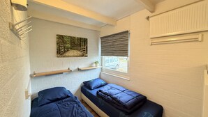 A small, compact room with two single beds, a shelf with a plant, a painting of a forest, and a window with blinds. - Bungalowpark Simpelveld - Schakel 22 (Simpelveld)